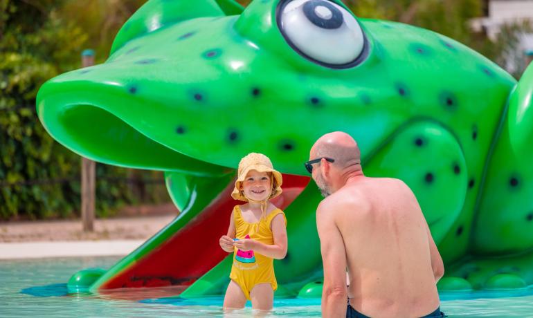 Enfant et adulte jouent dans une piscine avec une grenouille géante.