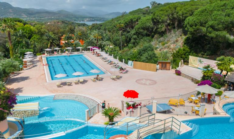 Piscine extérieure entourée de collines vertes et de parasols colorés.
