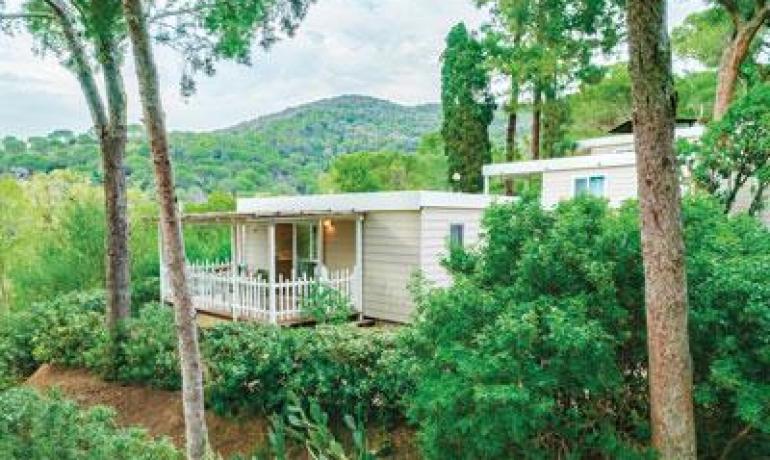 Casa mobile immersa nella natura con veranda, circondata da alberi e colline.