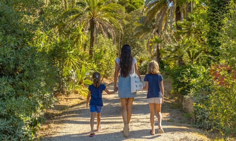 Persona e due bambini camminano in un giardino tropicale.