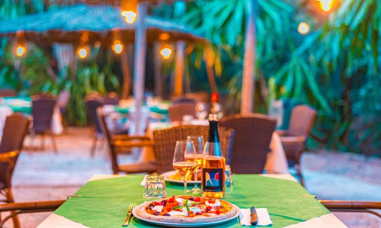 Cena romantica all'aperto con pizza e vino, luci soffuse e atmosfera tropicale.