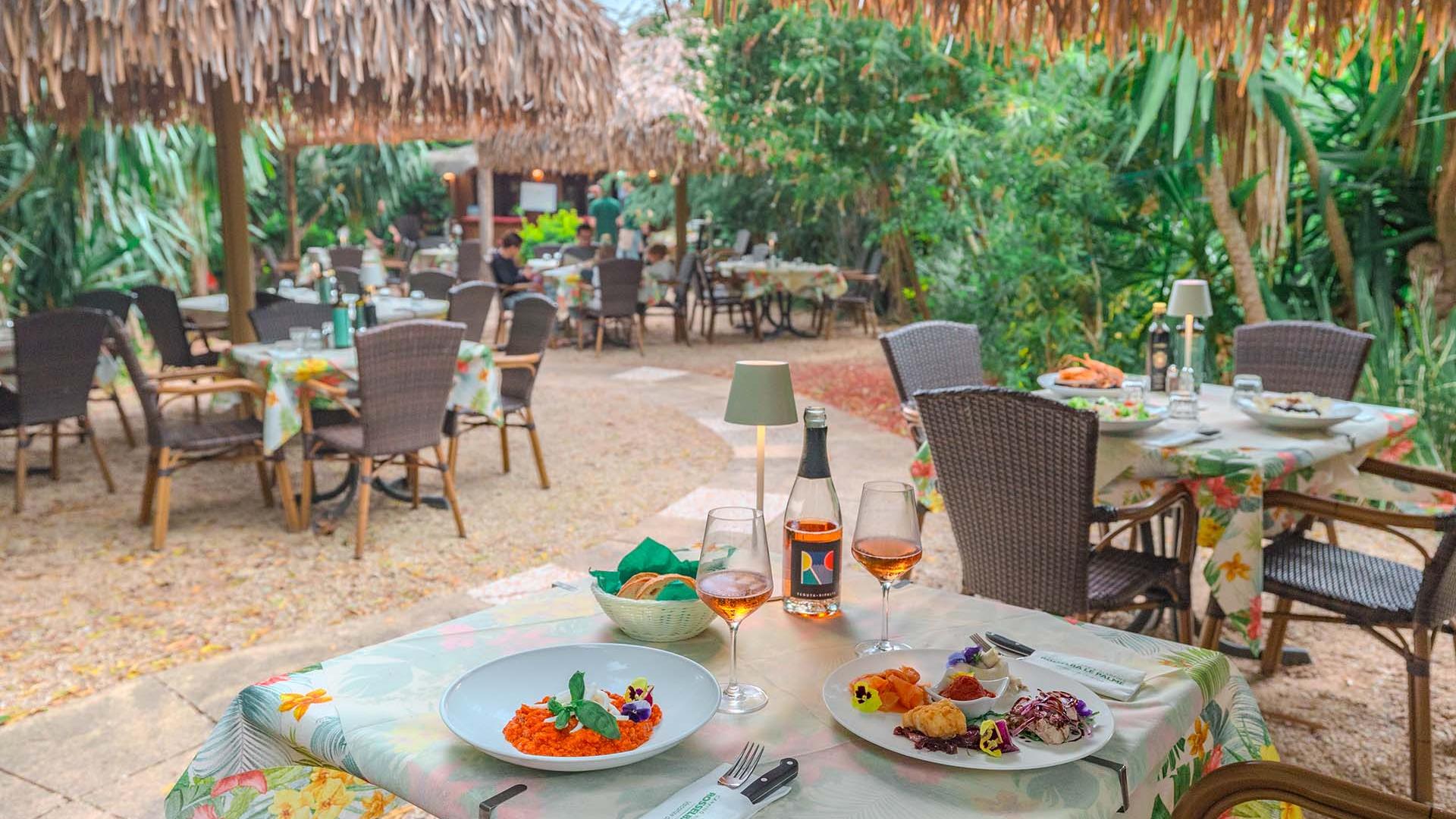 Restaurant en plein air avec plats gourmets et ambiance tropicale.